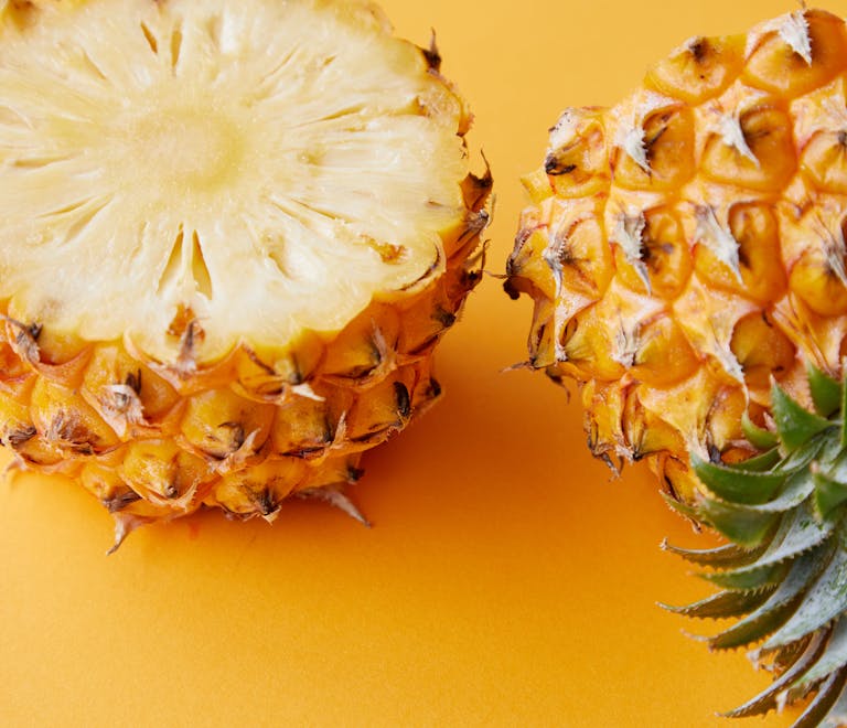 Close-up of juicy pineapple halves showcasing fresh tropical fruit on a vibrant yellow background.