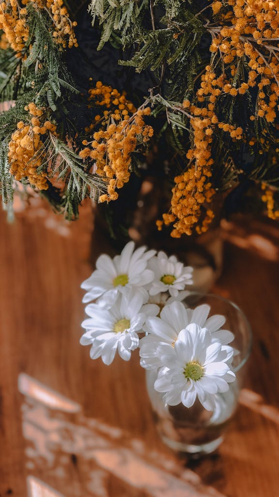 A vase with flowers and a yellow bush on a wooden table