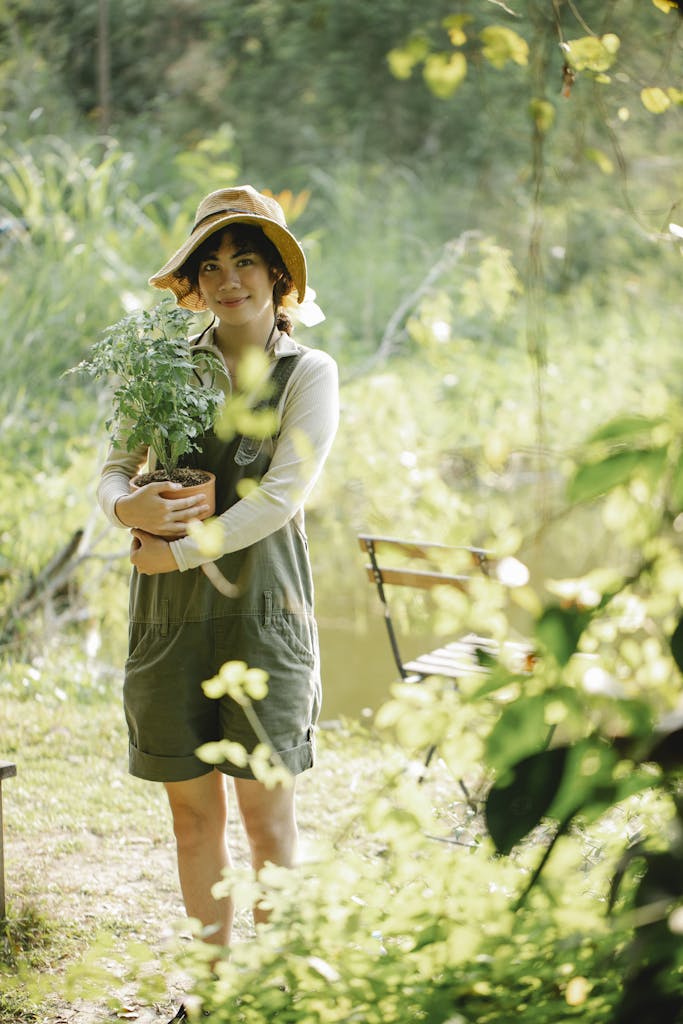 Smiling ethnic gardener with plant in sunlight